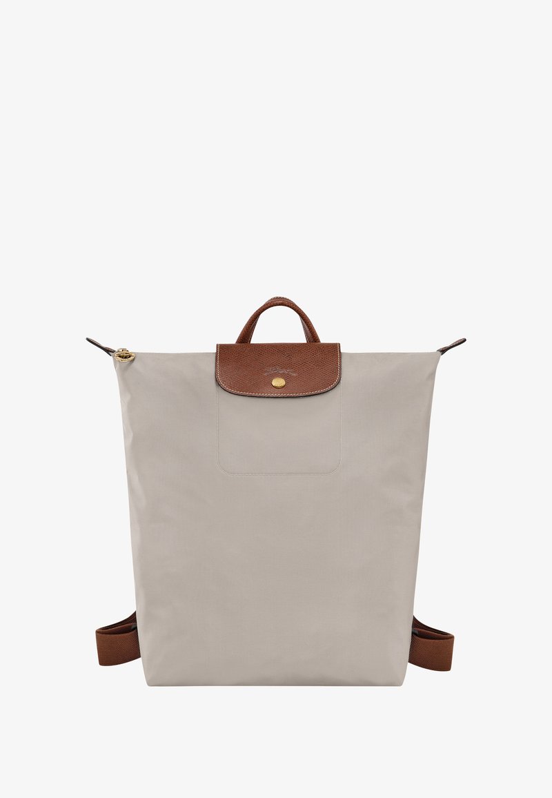 Beige nylon backpack with a textured brown leather flap and handle, gold hardware, and adjustable brown straps. Minimalist design.