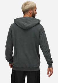 Sudadera de color gris oscuro con una textura suave, mangas largas, puños y dobladillo acanalados, que cuenta con una capucha grande y un diseño de ajuste relajado.