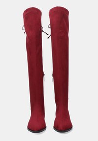 Par de botas altas de ante rojo con puntas afiladas, tacones de bloque, cremalleras laterales y detalle de cordones en la parte superior trasera.