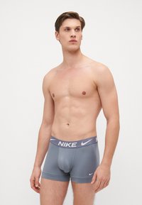 Graue Nike-Boxershorts mit einem kontrastierenden dunkelgrauen Bund, auf dem das Nike-Logo in Weiß abgebildet ist. Glattes Material mit enger Passform und minimalistischem Design.