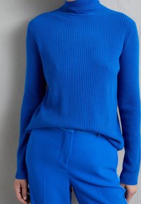 Pull à col roulé côtelé en bleu vif. Comporte des manches longues et une coupe décontractée, accompagné d'un pantalon assorti bleu.
