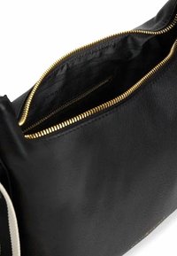 Borsa in pelle nera con texture liscia, cerniera dorata e fodera interna nera. Presenta un dettaglio a striscia a contrasto su un lato.