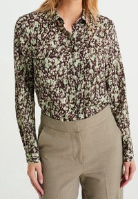 Blus med blommönster i gröna och bruna nyanser, knapplist, långa ärmar, mjukt tyg, med klassisk krage och avslappnad passform.