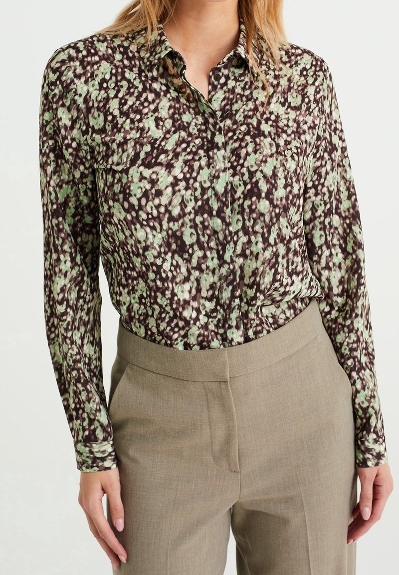 Blus med blommönster i gröna och bruna nyanser, knapplist, långa ärmar, mjukt tyg, med klassisk krage och avslappnad passform.