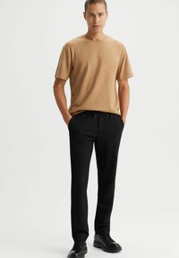 Beżowa bawełniana koszulka z okrągłym dekoltem, zestawiona z czarnymi spodniami na sznurki i czarnymi sznurowanymi butami. Prosty design, bez wzorów i wyrazistych akcentów.