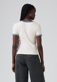 Hvit bomulls t-skjorte med lyseblå ribbestrikket krage og ermekanter, tettsittende design, parret med mørkegrå høyhalsa jeans.