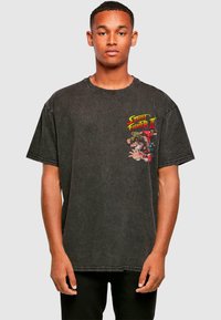 Sort oversized T-shirt lavet af bomuld. Har en farverig "Street Fighter II" grafik på venstre bryst. Korte ærmer og rund halsudskæring.
