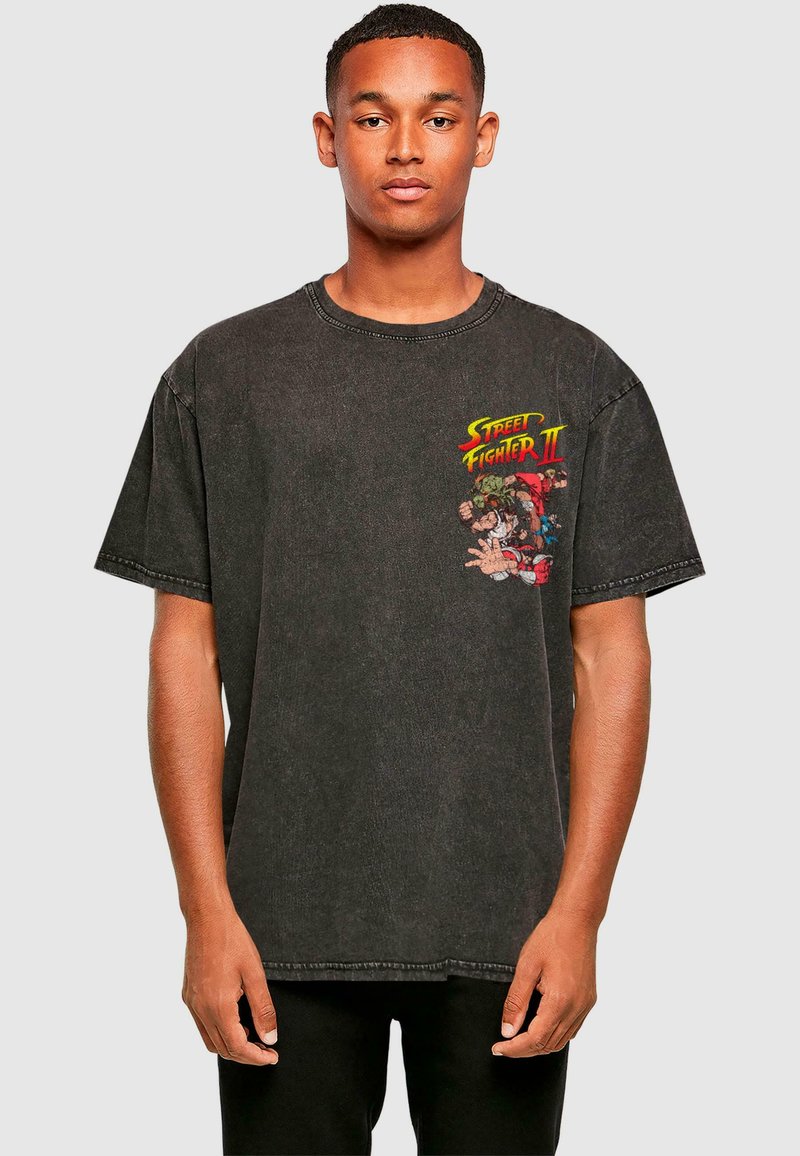 Sort oversized T-shirt lavet af bomuld. Har en farverig "Street Fighter II" grafik på venstre bryst. Korte ærmer og rund halsudskæring.