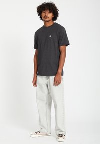 Grijze katoen t-shirt met een ronde halslijn en een klein logo op de borst, gecombineerd met lichtgrijze denim jeans en sneakers met zwarte accenten.