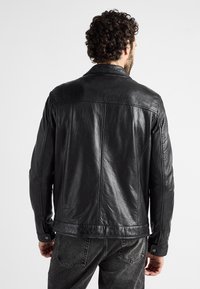 Zwarte leren jas met een gestructureerde afwerking, voorzien van een puntige kraag, zichtbare naden en drukknopen. Klassiek recht gesneden ontwerp.