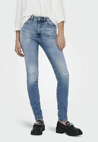 Vaqueros de mezclilla ajustados de color azul claro con detalles rasgados, cinco bolsillos y una cintura de altura media. Combinados con zapatos de plataforma negros.