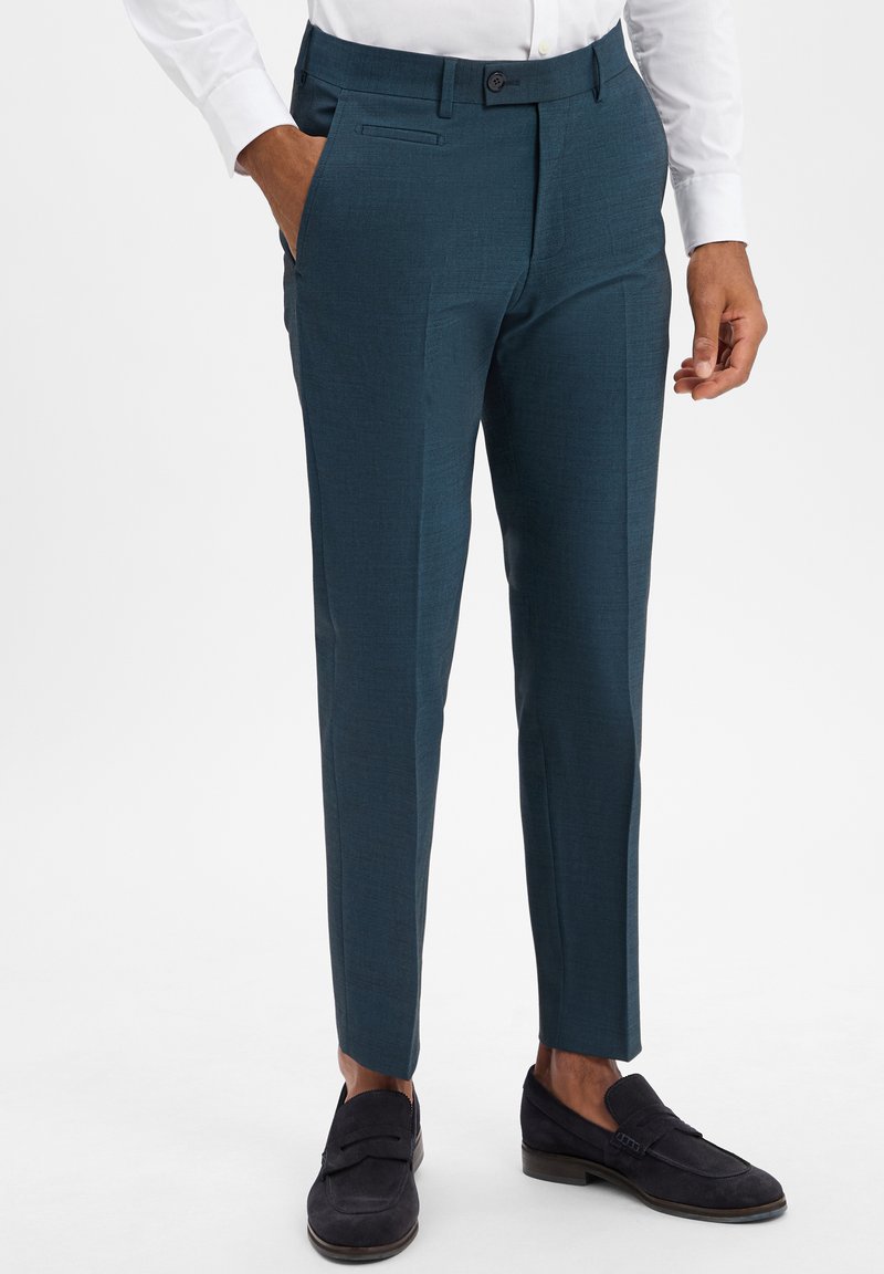 Türkise, taillierte Anzughosen aus strukturiertem Stoff mit flachem Bund, seitlichen Taschen und Gürtelschlaufen, kombiniert mit dunklen Slippern.