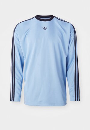 Light blue long-sleeve shirt with black accents and three stripes along sleeves, featuring a small black logo on the chest. Soft fabric texture.
