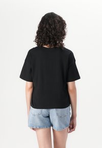 T-shirt noir à manches courtes en coton, avec une coupe décontractée et un design simple. Porté avec un short en jean bleu clair.