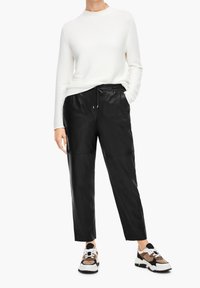 Pantalons en cuir noir avec une taille à cordon, associés à un pull en côte blanc. Les chaussures présentent une semelle épaisse avec des accents beiges et noirs.