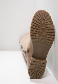 Botín beige hasta el tobillo con un upper de cuero liso y puntera redonda, que cuenta con una suela de goma texturizada y detalle de cremallera lateral. Talla 37.