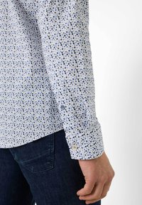 Weißes Hemd mit blauem Punktmuster, aus Baumwolle, mit langen Ärmeln, Knopfmanschetten und geradem Saum, getragen mit dunklen Denim-Hosen.