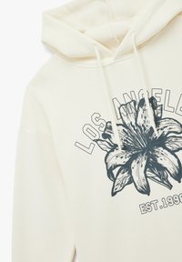 Felpa con cappuccio crema caratterizzata da una grafica frontale di un fiore e il testo "Los Angeles". Presenta lacci e una texture morbida.