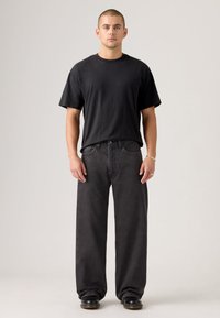 Black short-sleeve t-shirt paired with wide-leg black denim jeans. Smooth fabric texture, minimalist design, and subtle stitching details.