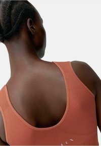 Geribbelde sporttanktop in gebrand oranje, met een lage scooprug en subtiele logodetail op de stof. Zacht, rekbaar materiaal.