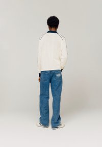 Pull crème tricoté avec un col marin et des rayures noires sur les côtés ; associé avec un jean en denim bleu clair et des baskets blanches avec des accents noirs.