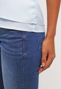 Haut sans manches bleu clair avec une finition satinée lisse, associé à un jean en denim bleu foncé à coupe slim et texture subtile.