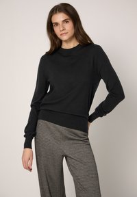 Maglione nero con maniche lunghe e scollo rotondo, abbinato a pantaloni grigi con motivo. Tessuto liscio e design aderente.