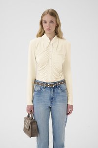 Langermet kremfarget bluse med knepping foran og rynkedetalj. Kombinert med høytlivs lyseblå jeans og en grå veske.
