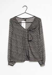 Blusa gris de manga larga con escote en V y lazo frontal. Presenta un estampado de lunares y puños elásticos. Está hecha de una tela ligera y texturizada.