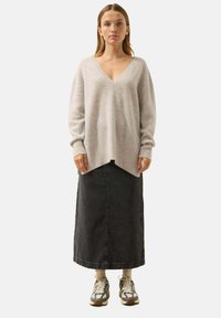 Lichtgrijze, geribbelde gebreide trui met een V-hals en lange mouwen, gecombineerd met een donkere spijkerrok en gemusterde sneakers.