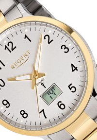 Montre argentée avec un bezel en or, cadran blanc, index horaires noirs et aiguilles dorées. Présente un affichage numérique en bas affichant la température.