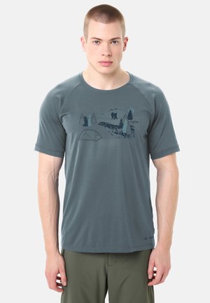 Giovane uomo che indossa una t-shirt da escursionismo grigia con una grafica della natura che mostra escursionisti, alberi, una tenda e montagne.