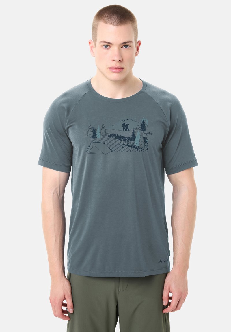 Giovane uomo che indossa una t-shirt da escursionismo grigia con una grafica della natura che mostra escursionisti, alberi, una tenda e montagne.