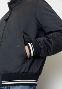 Bomber jacket blu navy con colletto alla coreana, due tasche laterali, polsini a costine con strisce bianche e vita elastica. Tessuto liscio.