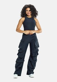 Black crop top and fitted cargo pants with ruffled details and multiple pockets. Smooth fabric and athletic cut, paired with white shoes.