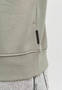 Lysegrå sweatshirt med blød tekstur, der har ribbede manchetter og kant samt et lille mørkt stofmærke med "JACK & JONES" på siden.