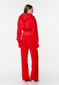 Czerwony krótki hoodie z kapturem i długimi rękawami, w zestawie z czerwonymi szerokimi spodniami. Miękka tkanina o gładkiej fakturze, minimalne detale.