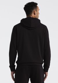 Zwarte hoodie met een zachte textuur, voorzien van een ruime capuchon en ribbelmanchetten. Het ontwerp heeft een ontspannen pasvorm en minimale naden.
