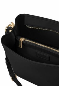 Intérieur d'un sac à main en cuir noir avec une fermeture éclair dorée et un compartiment zippé séparé. Design simple et texture lisse.