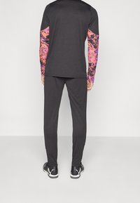 Schwarzes Sportoutfit mit einem Langarmtop, das bunte, abstrakt gemusterte Ärmel hat, und passenden schwarzen Hosen. Strukturierter Stoff.