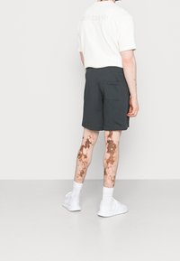 Tmavě šedé, texturované kraťasy s kapsou na zadní straně, nošené s bílým, proužkovaným tričkem s krátkým rukávem a bílými teniskami.