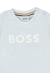 Jasnoniebieska bawełniana koszulka z dużym białym logo "BOSS" z przodu. Okrągły dekolt z dwoma zatrzaskami na ramieniu.