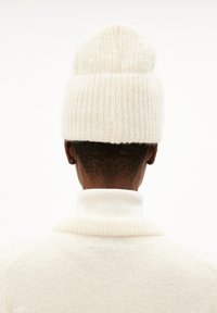 Crème-kleurige gebreide beanie met een ribbelstructuur, gedragen met een bijpassende crème coltrui. Zacht en gezellig uiterlijk.