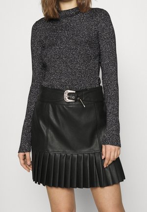 Femme portant un haut à manches longues noir pailleté et une jupe plissée noire en similicuir avec une large ceinture et une boucle argentée.