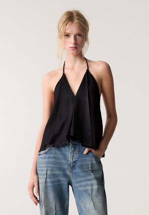 Crna satenska halter top s dubokim V-izrezom, lepršavim A-linijskim dizajnom i laganom teksturom. Uparen s plavim iznošenim trapericama.