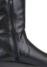 Bota de cuero negra con cremallera lateral, textura suave y diseño estructurado, con suela de goma gruesa y detalles de costura.