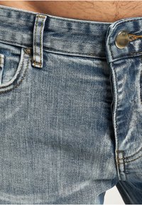 Lyseblå denimjeans med klassisk fem-lommers design, med synlige sømmer, en metallknapp og litt falmet tekstur.