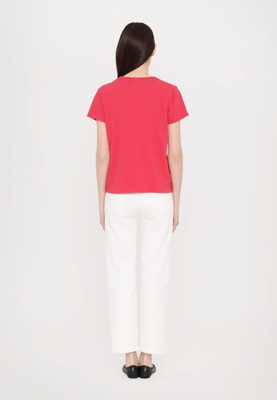 Red short-sleeve t-shirt made of cotton, paired with white wide-leg trousers. Rear view shows simple design and no visible logos or patterns.