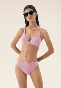 Jasnoróżowy zestaw bikini z teksturowanej tkaniny. Góra ma trójkątny fason z cienkimi ramiączkami, a dół to bikini o średnim stanie.