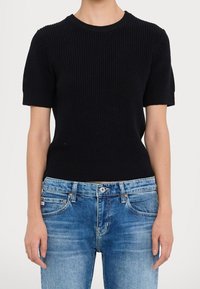 Pull noir côtelé en maille à manches courtes avec un col rond, associé à un jean bleu délavé avec un design classique à cinq poches.